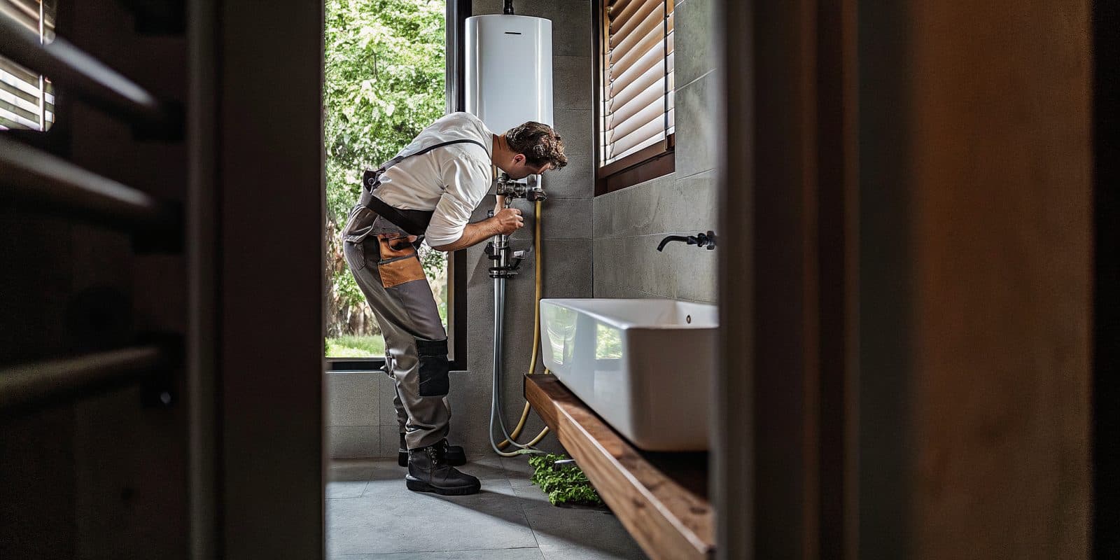 Mend plumber repairing pipework beneath a bathroom water heater in an Austin-area home